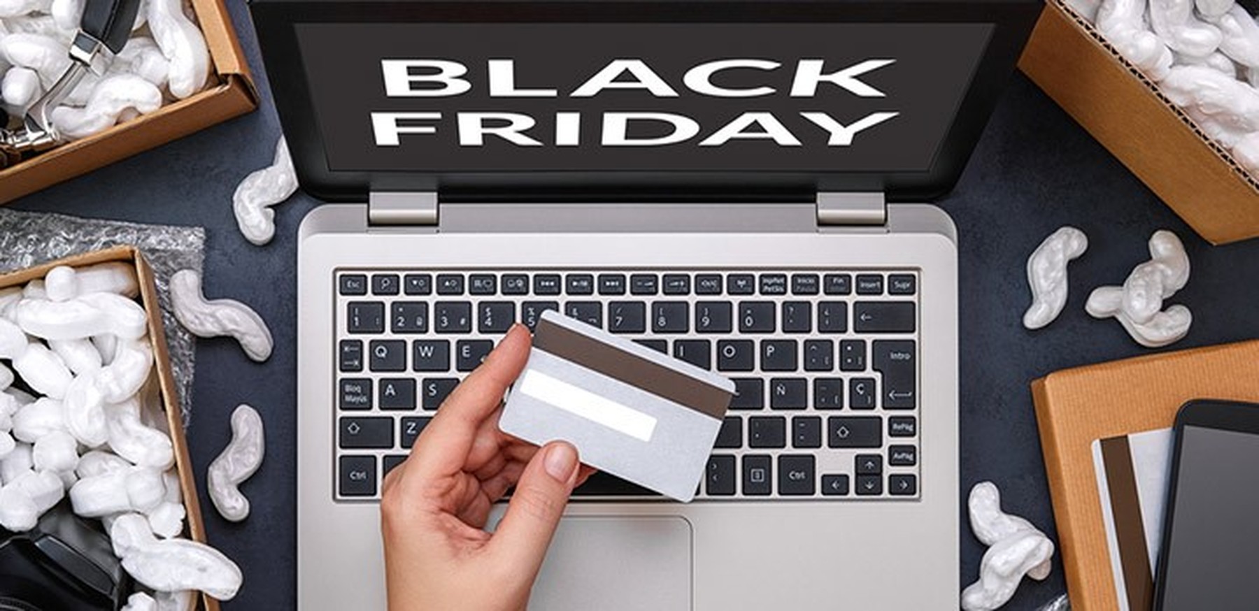 ordenador portátil con Black Friday en la pantalla, una persona con una tarjeta de crédito y cajas de pedidos alrededor