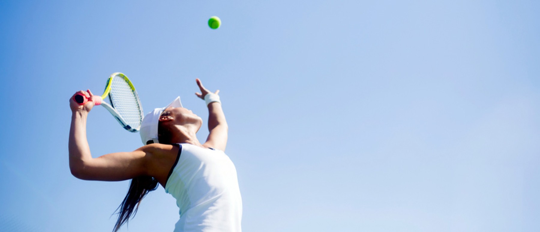 eine Frau in Weiß die unter blauem Himmel Tennis spielt