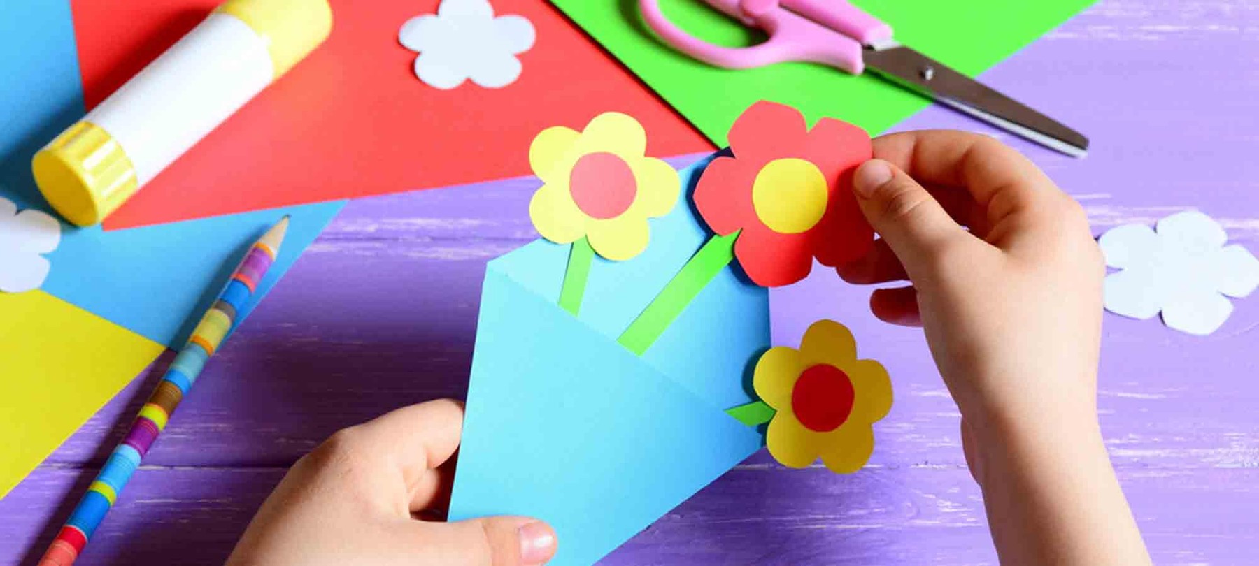 A child puts together a bouquet of flowers made from coloured paper