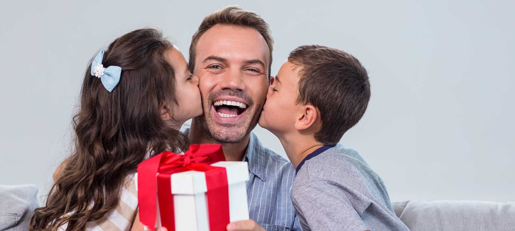 Two kids are giving their dad a present while they're both kissing him on each cheek